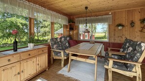 Eine Holzhütte mit Esstisch, zwei Stühlen, einem Schrank und einem Fenster mit Blick ins Freie.