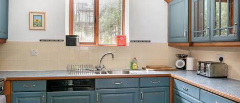 A kitchen with teal cabinets, a window with a view, a sink, and a toaster.