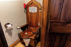 A wooden toilet with a plaque, a red candle, and a toilet paper holder.