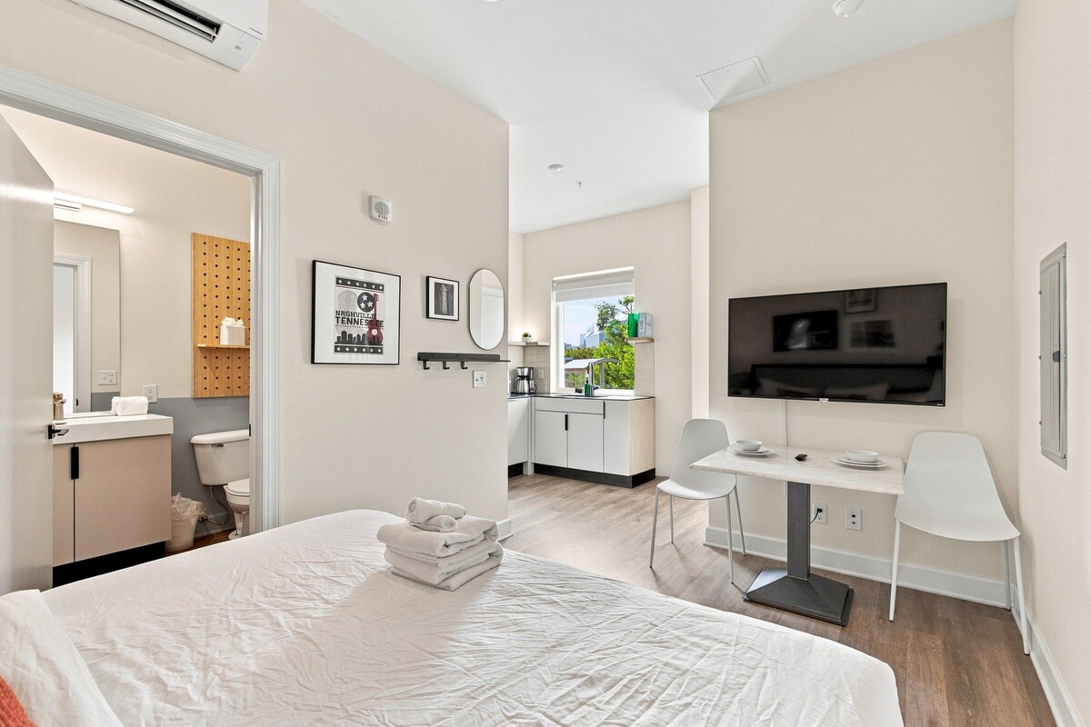 A modern hotel room with a bed, a TV, a desk, and a bathroom.