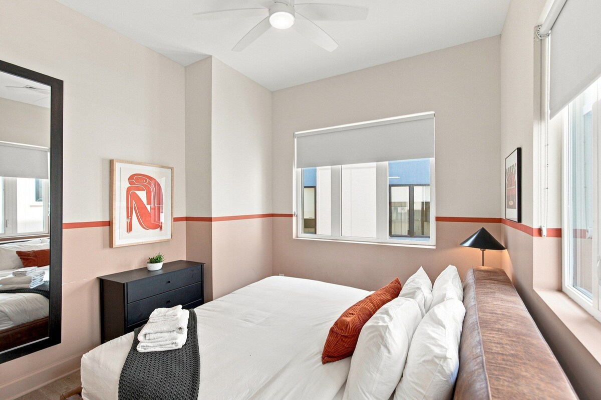 A hotel room with a bed, a desk, a chair, a mirror, and a window.