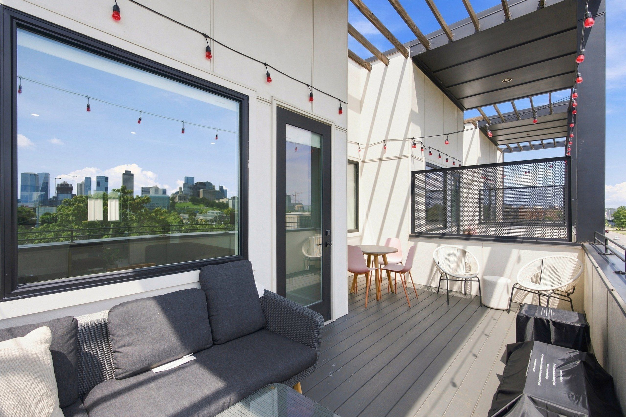 A modern balcony with a sofa, chairs, and a table, overlooking a cityscape.