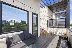 A modern balcony with a sofa, chairs, and a table, overlooking a cityscape. - The Conway (Nashville)