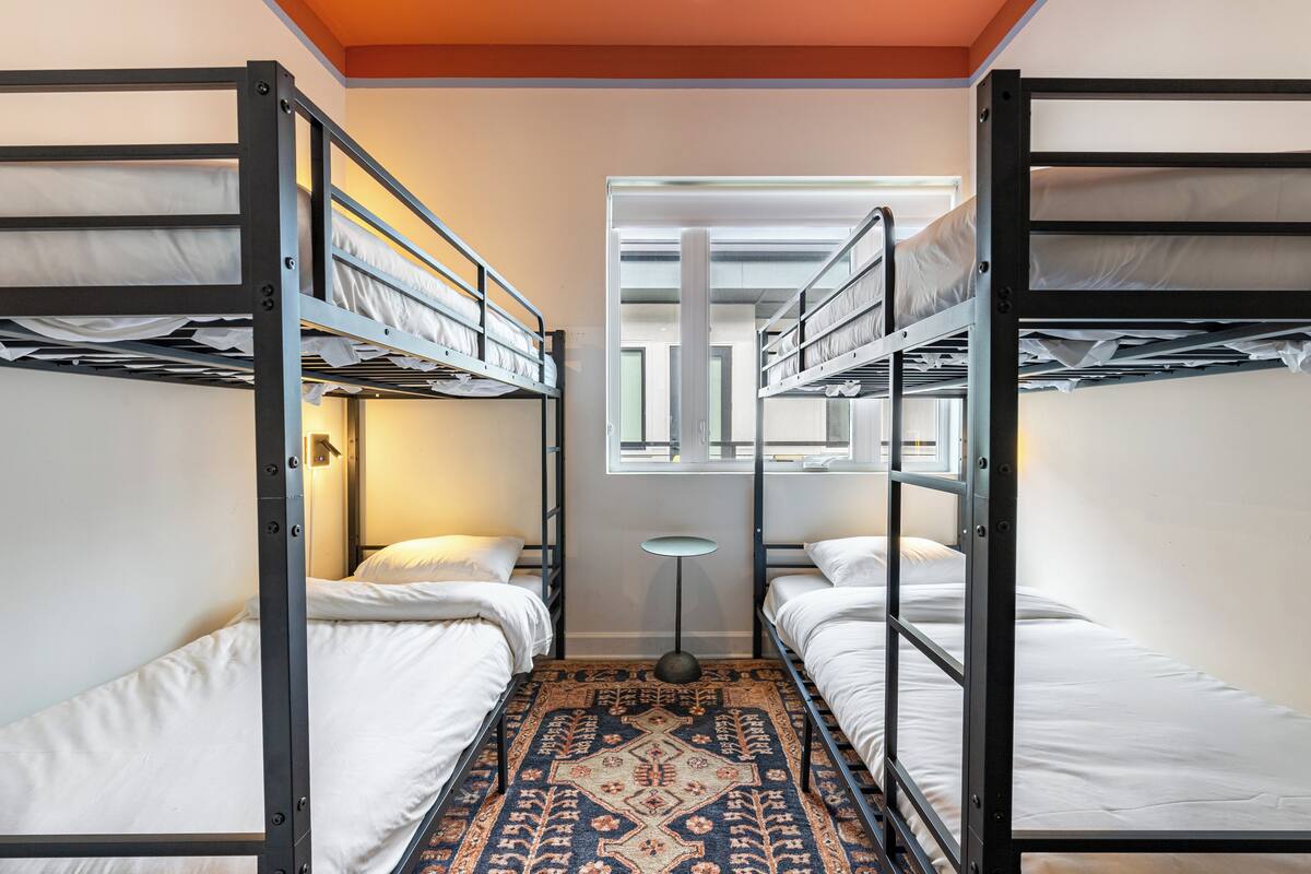 A room with bunk beds, a patterned rug, and a small table with a lamp.