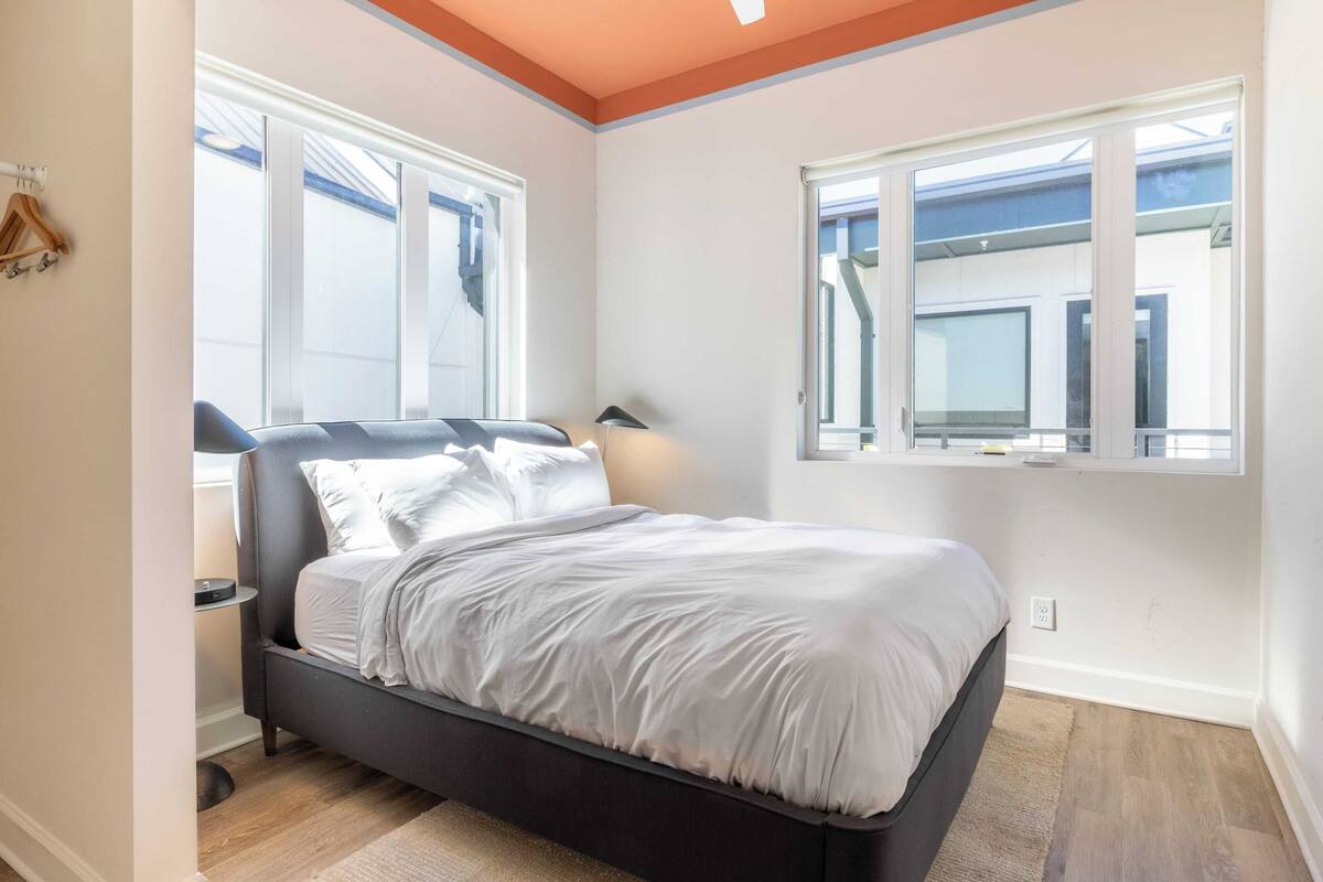 A bedroom with a bed, two windows, a nightstand, and a lamp.