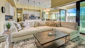 A spacious living area with a large sectional sofa, a wooden coffee table, and a view of the kitchen and balcony. - Amazing Octopus | Pool | Spa | outdoor Bar | Office (Placida)