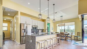 A modern kitchen with a central island, bar stools, and a dining area with a view. - Amazing Octopus | Pool | Spa | outdoor Bar | Office (Placida)