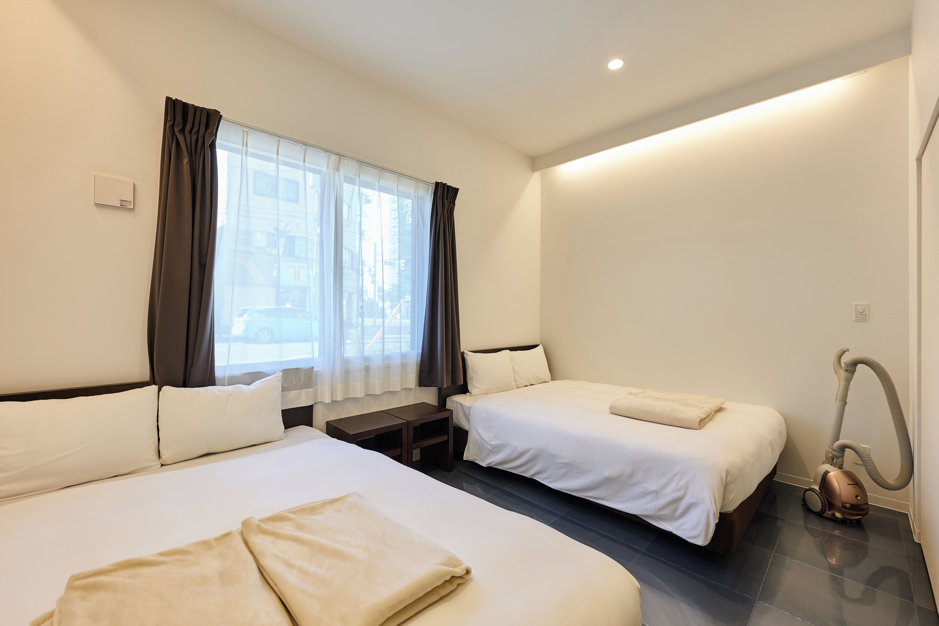 Habitación de hotel con dos camas, una mesita de noche, una ventana con cortinas y una aspiradora.