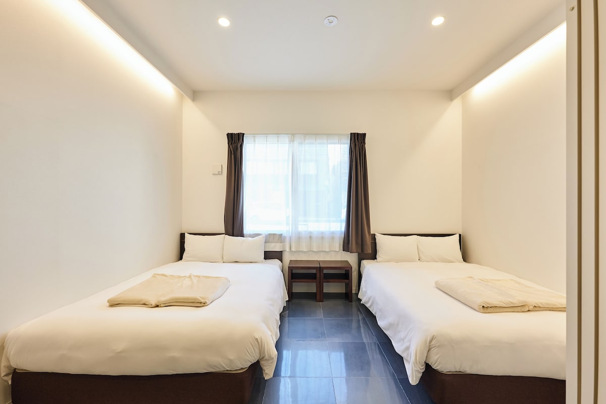 A hotel room with two beds, a small table, and a window with curtains.