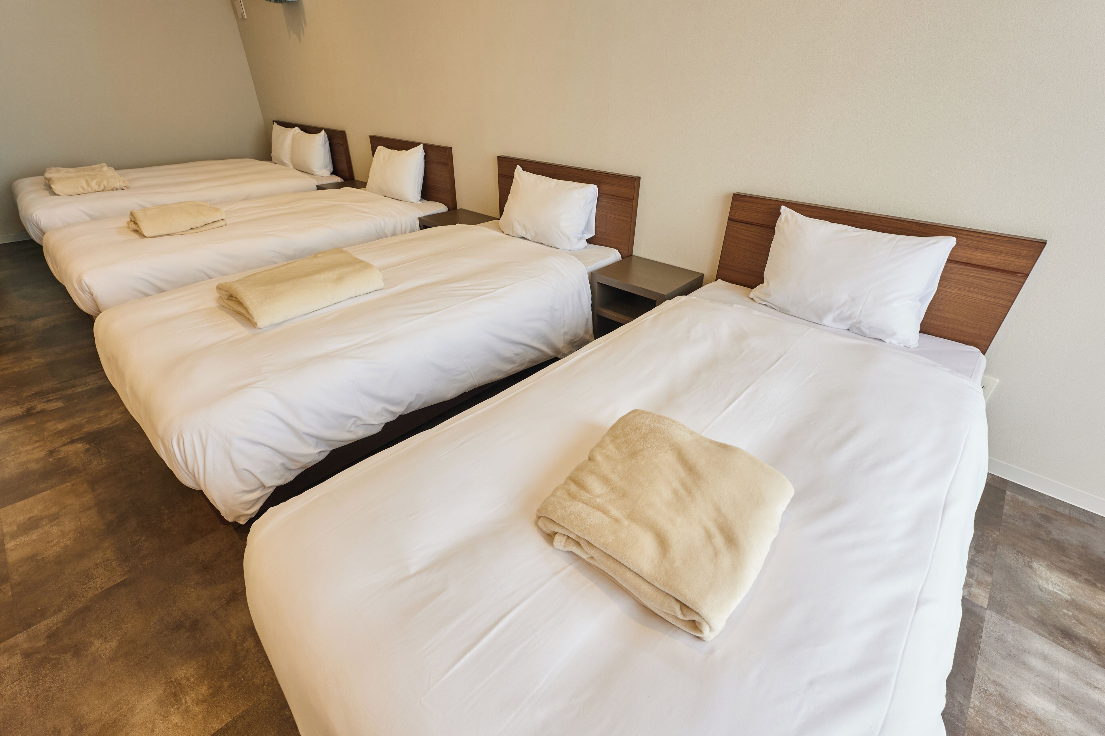 Habitación de hotel con cuatro camas individuales, cada una con cabecero de madera y ropa blanca.