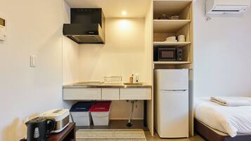 A compact kitchenette with a microwave, stove, sink, and storage cabinets. A refrigerator is adjacent to the kitchenette, and a bed is visible in the background.