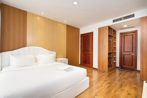 Ein Schlafzimmer mit einem großen Bett, Holzwandverkleidung, einem Kleiderschrank und einer Tür zu einem Abstellraum.