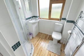A bathroom with a wooden floor, white tiles, a window, a sink, a toilet, and a shower. - The Dormers - Amazing Views & Space (Stroud)