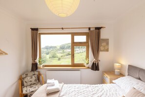 A bedroom with a large window, a chair, a bedside table with a lamp, and a bed. - The Dormers - Amazing Views & Space (Stroud)