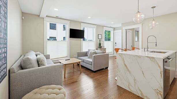 A modern living room with a sofa, a coffee table, and a TV mounted on the wall. - Inviting 3BR In Cambridge, Walk To T & Central Sq (Cambridge)