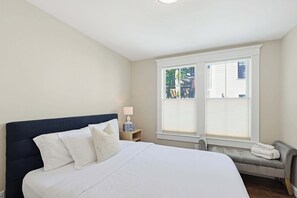 Une chambre à coucher comprenant un lit, une table de chevet, une lampe, une fenêtre et un banc.