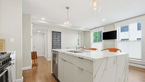 A modern kitchen with a marble island, stainless steel appliances, and pendant lighting. - Inviting 3BR In Cambridge, Walk To T & Central Sq (Cambridge)