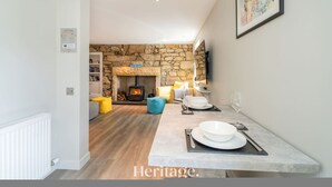 Un salon moderne avec un mur en pierre, une cheminée et un coin repas avec une table mise pour deux personnes.