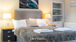 Un dormitorio con una cama grande, dos mesitas de noche con lámparas, un estante en la pared y una obra de arte enmarcada sobre la cama.
