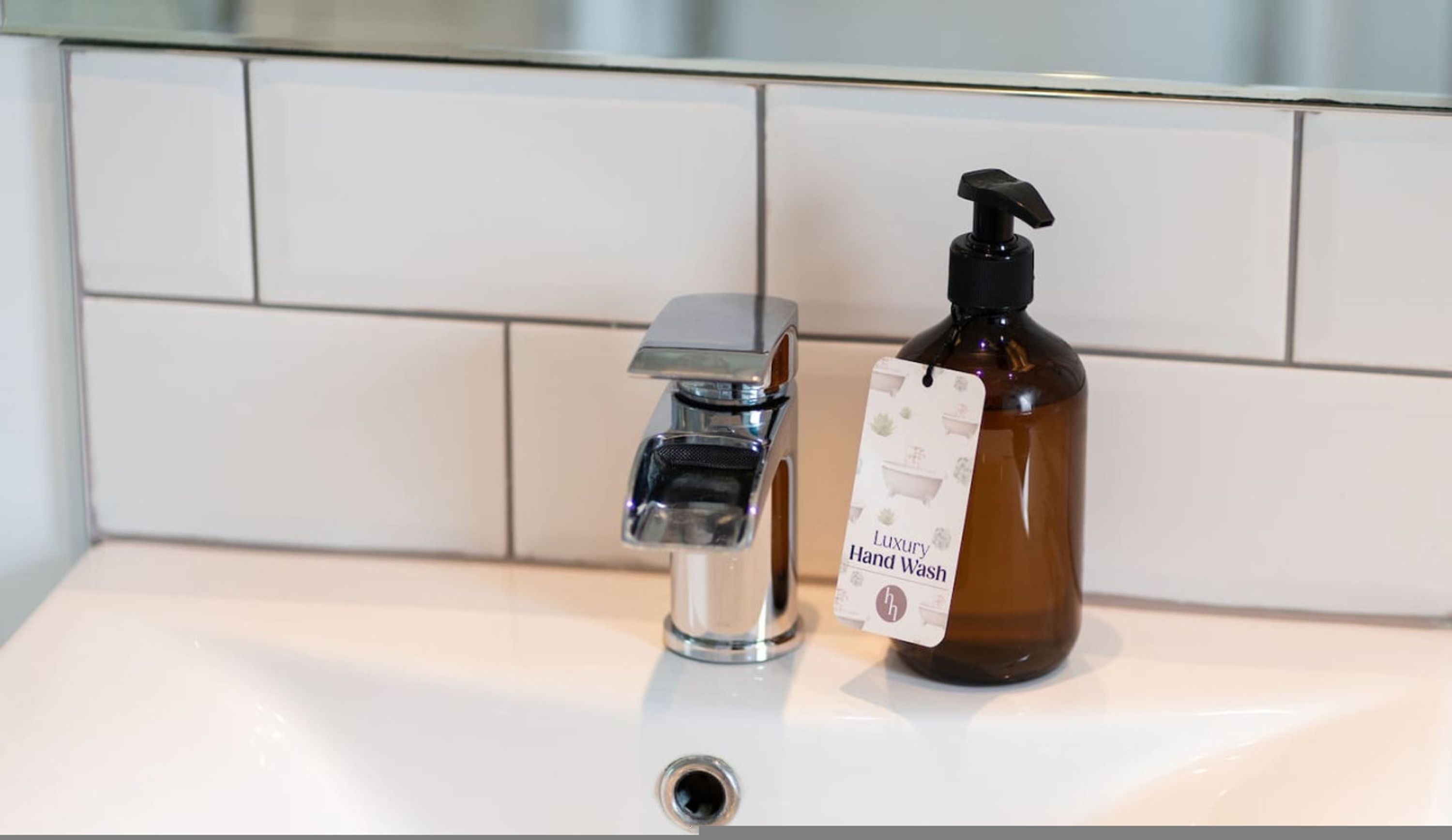 Ein Badezimmerwaschbecken mit einem Chromarmaturen und eine braune Handseifenflasche mit einem Etikett.