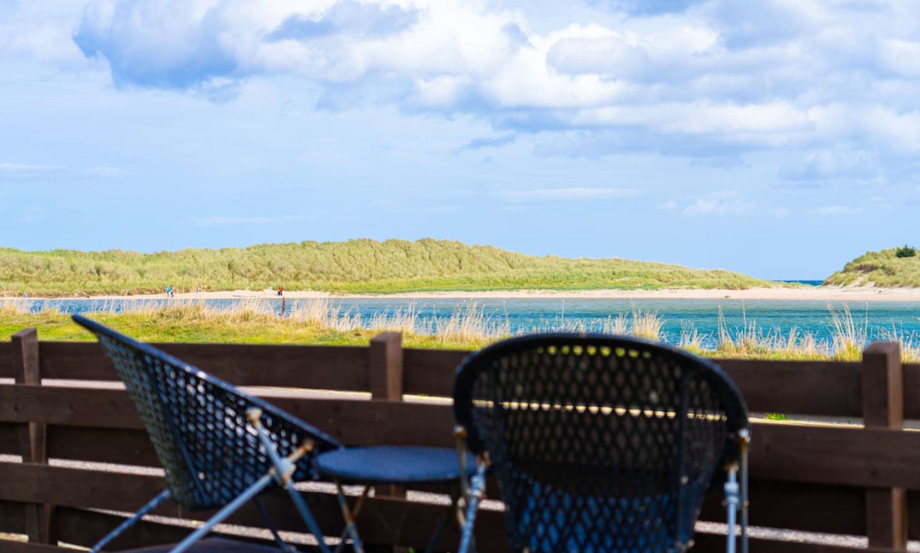 A view of a beach with two folding chairs and a wooden fence.