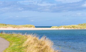 A coastal landscape with a sandy beach, grassy dunes, and a calm body of water. - Beach Cottage Pet Child Friendly Stay in Moray (Lossiemouth)