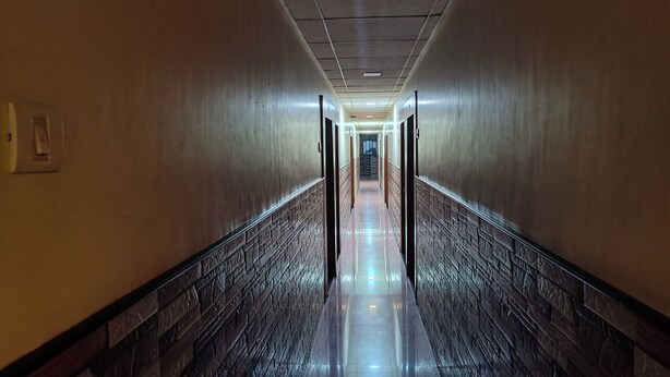 A long, well-lit hallway with a polished floor and textured walls, leading to a staircase at the end. - Trio hotel (Vasai)