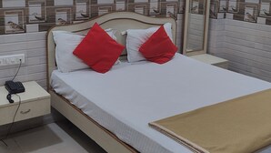 A neatly made bed with white and red pillows, a bedside table with a phone, and a beige throw blanket. - Trio hotel (Vasai)