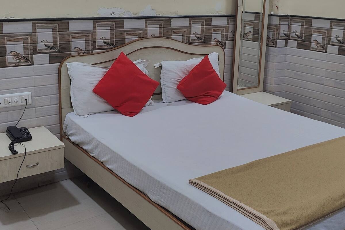 A neatly made bed with white and red pillows, a bedside table with a phone, and a beige throw blanket.