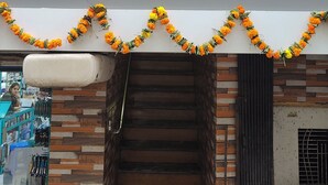 A hotel entrance with a staircase leading up to the door, a signboard with the hotel name, and a garland of marigold flowers above the entrance. - Trio hotel (Vasai)