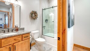 A modern bathroom with a granite countertop, wooden cabinets, a white toilet, a glass shower enclosure, and a framed picture on the wall. - Ski Season Escape! Fraser Condo & Hot Tub (Fraser)