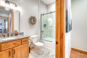 A modern bathroom with a granite countertop, wooden cabinets, a white toilet, a glass shower enclosure, and a framed picture on the wall. - Ski Season Escape! Fraser Condo & Hot Tub (Fraser)