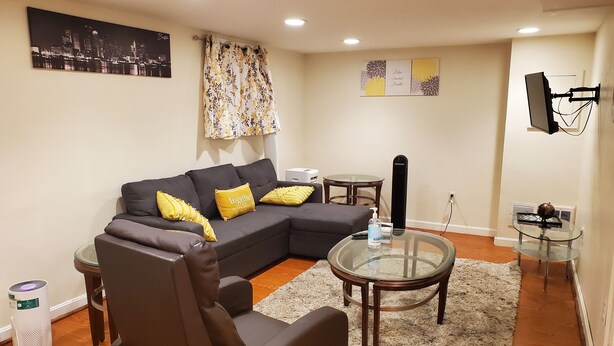 Una sala de estar con un sofá modular, una mesa de centro de vidrio, una mesita redonda y un televisor montado en la pared.