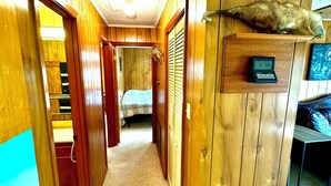 A hallway with wooden walls and doors, a bed in the background, and a digital clock on a wooden panel. - Spacious 4-bedroom house in charming Rockport with AC, WiFi BAR  (Rockport)