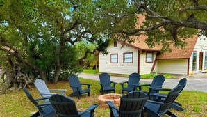 A group of Adirondack chairs arranged around a fire pit in a grassy outdoor area with trees and a building in the background. - Spacious 4-bedroom house in charming Rockport with AC, WiFi BAR  (Rockport)