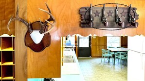 A kitchen with wooden cabinets, a dining area with a table and chairs, and a wall-mounted deer head with antlers. - Spacious 4-bedroom house in charming Rockport with AC, WiFi BAR  (Rockport)