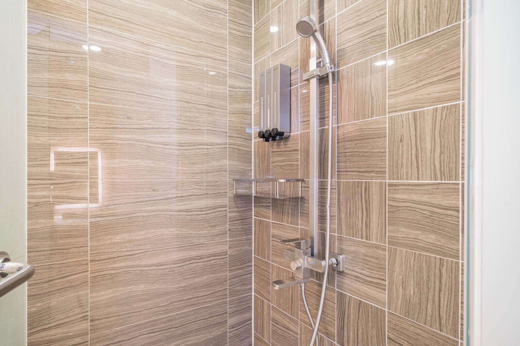 Un baño moderno con zona de ducha, paredes de azulejos y mampara de vidrio.