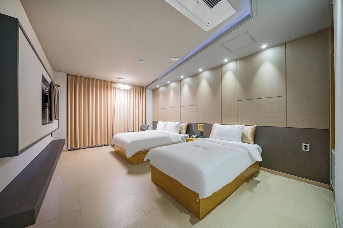 Habitación de hotel con dos camas, televisión y un ventanal grande con cortinas.