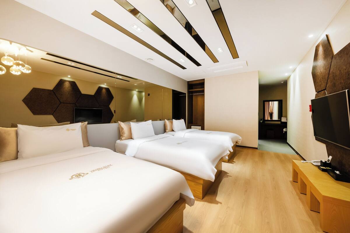 Habitación de hotel con dos camas grandes, un banco de madera, un televisor y un diseño moderno en el techo.