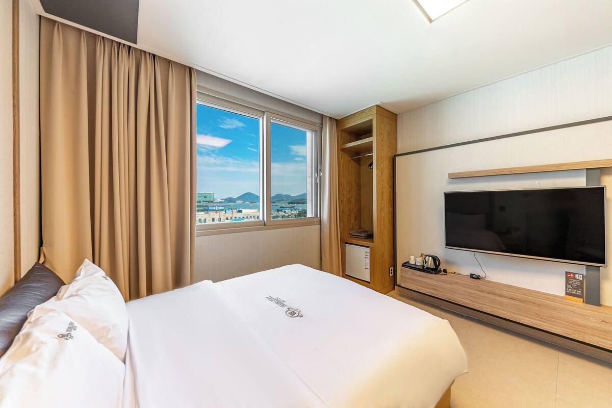 Habitación de hotel con una cama grande, televisión, armario de madera y vistas a la ciudad.