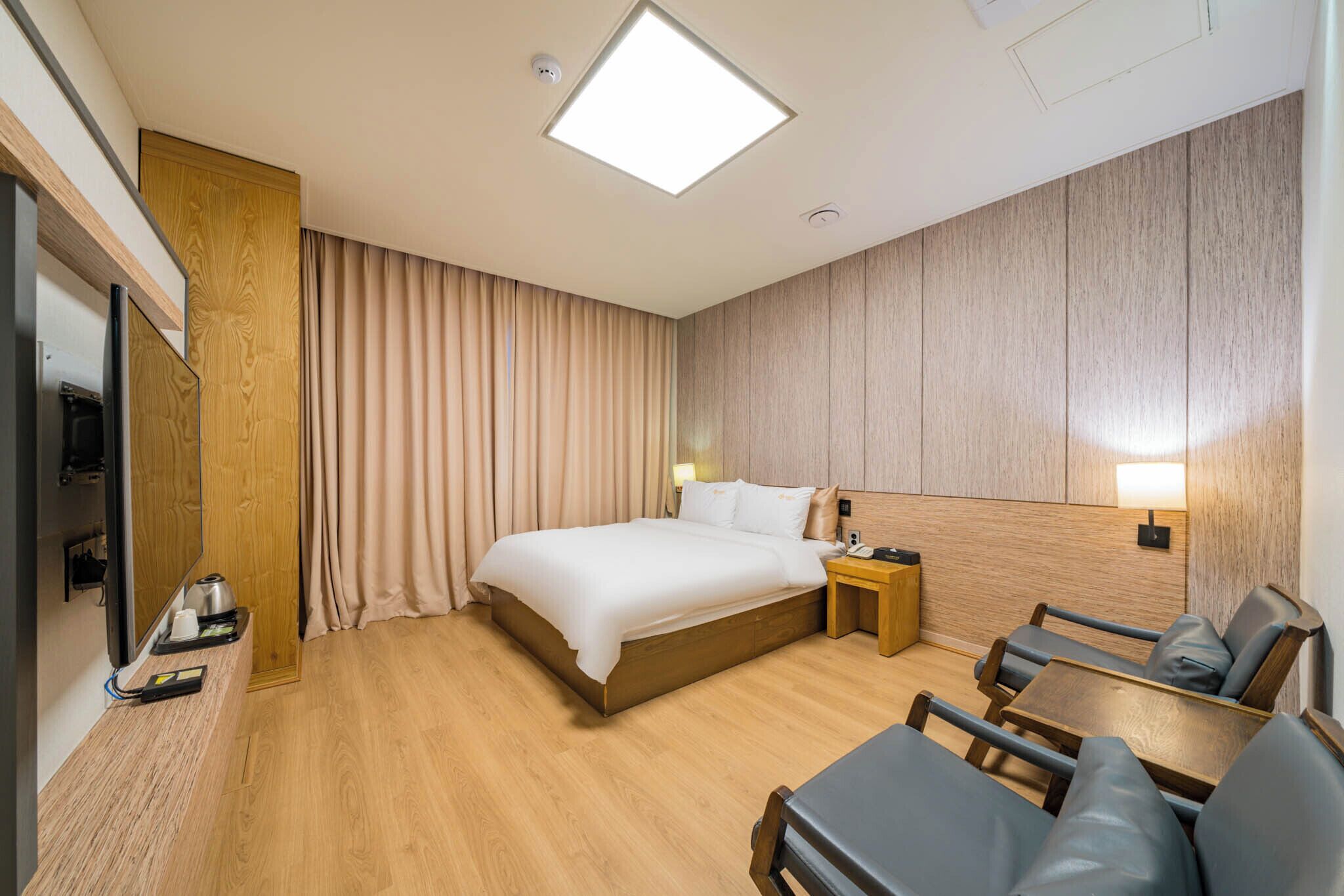 A hotel room with a large bed, a desk, a chair, a TV, and a wooden wardrobe.