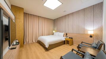 A hotel room with a large bed, a desk, a chair, a TV, and a wooden wardrobe.