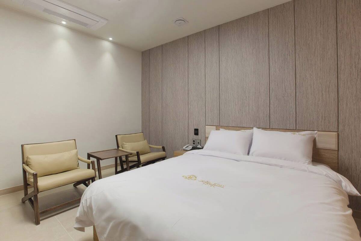 Habitación de hotel con cama, dos sillas, una mesita y un teléfono en la pared.