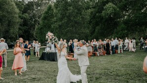 A wedding ceremony outdoors with guests seated on benches.