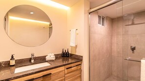 Features a large mirror, sleek countertop, and walk-in shower with handheld showerhead.