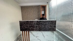 Zona de recepción con mostrador de mármol, pared con diseño y separador de vidrio texturizado.