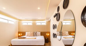 Two single beds with white linens and decorative pillows, a large mirror, and neutral decor.