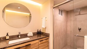 Bathroom features a sink with a chrome faucet, a large round mirror, and a glass-enclosed shower with a handheld showerhead.