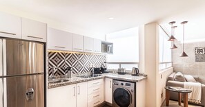 Enjoy a compact kitchen with stainless steel appliances, a dining area, and a living space with a sofa and city view.