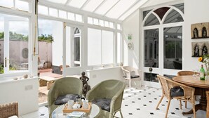 A conservatory with wicker furniture, a glass table, and a view of the garden. - Grade II Listed House in Central Exeter (Exeter)